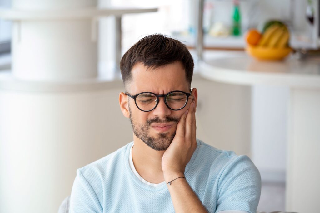 Man with brown hair in light blue shirt holding hand to jaw in pain